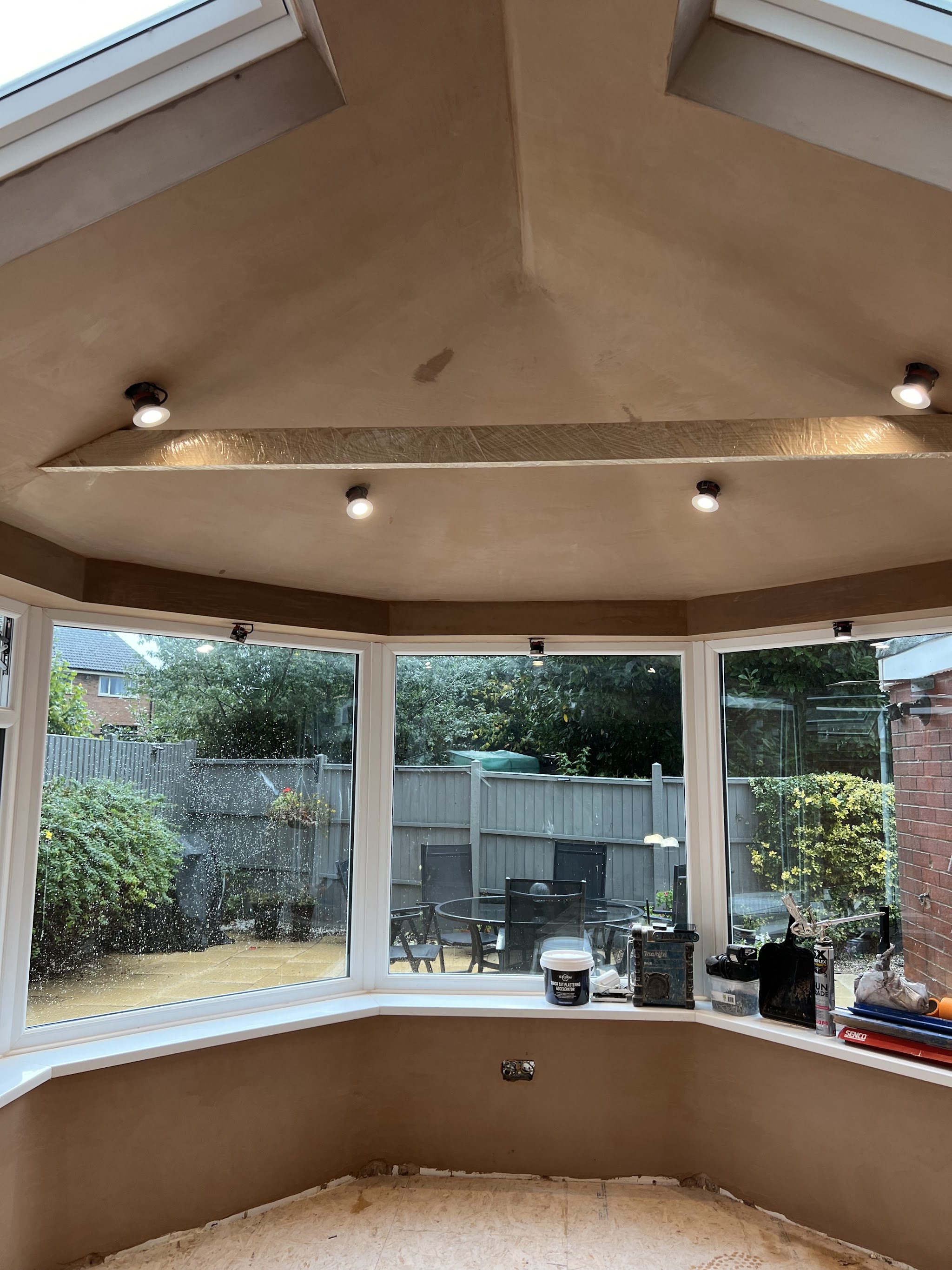 A conservatory ceiling freshly skimmed, with downlights and a bay of windows