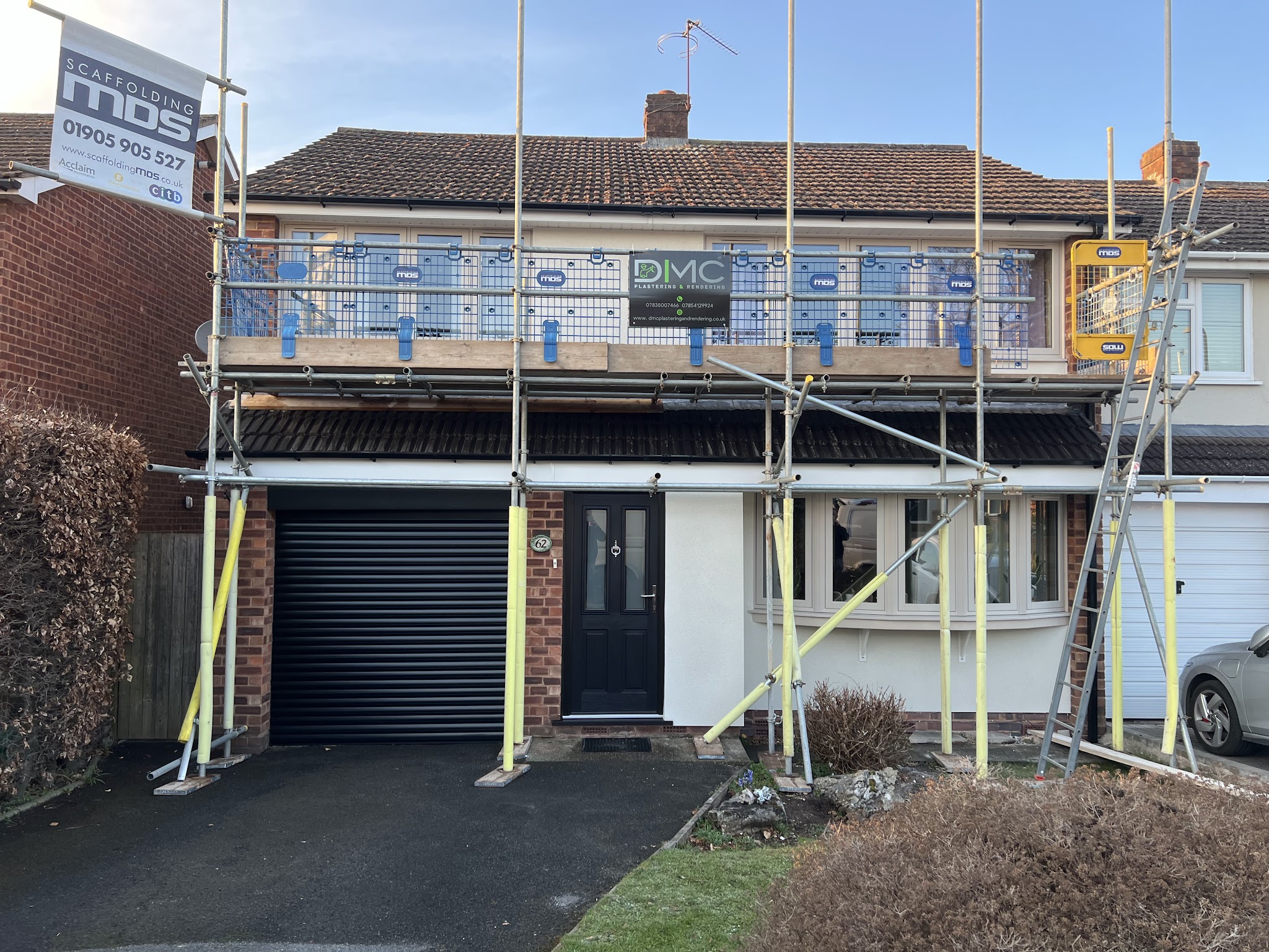 A house on scaffold with the DMC Plastering & Rendering banner fixed to the rail