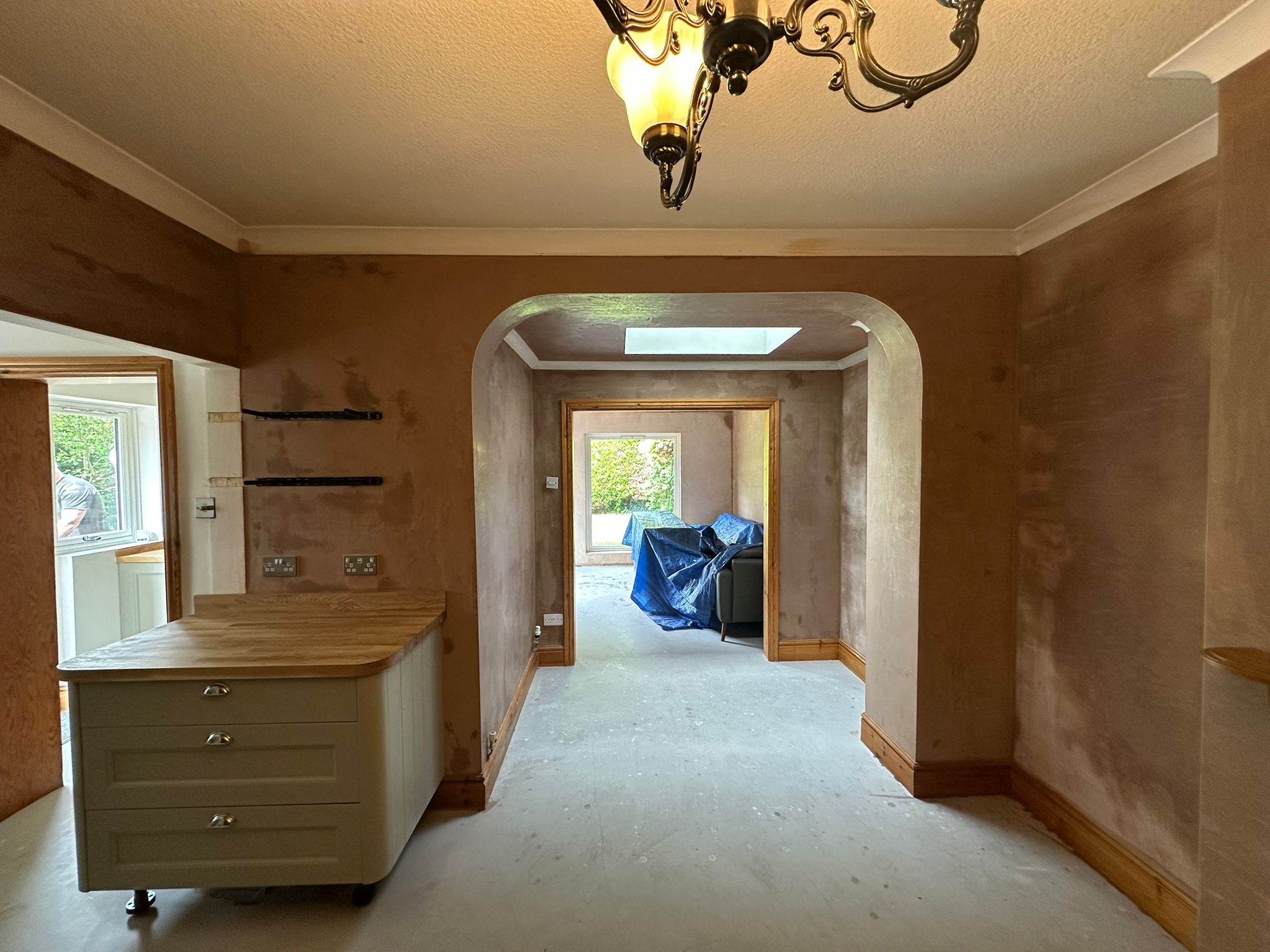 A kitchen and hallway with fresh plaster on the walls and an arched opening