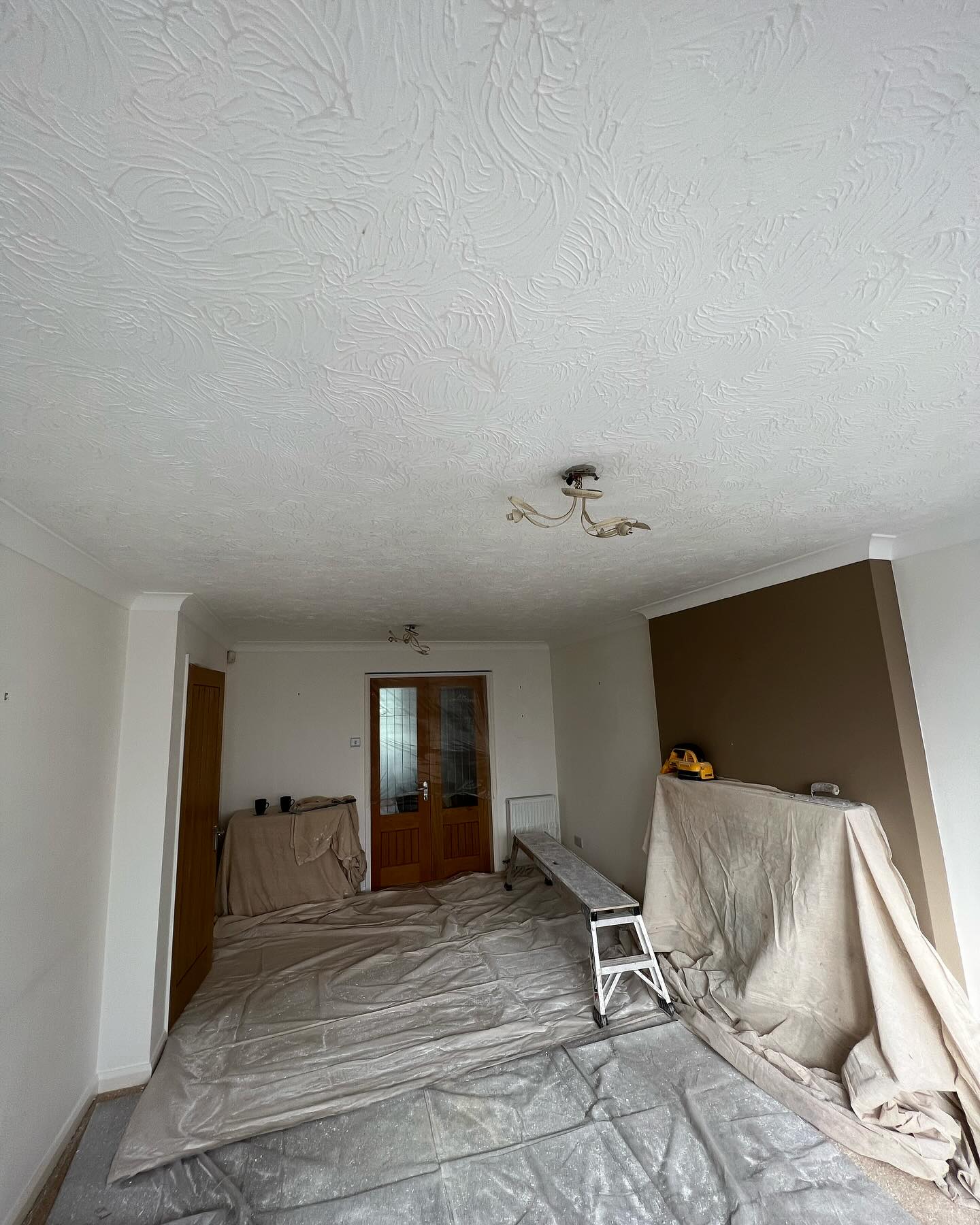 A room with a textured ceiling and dust sheets laid out before plastering
