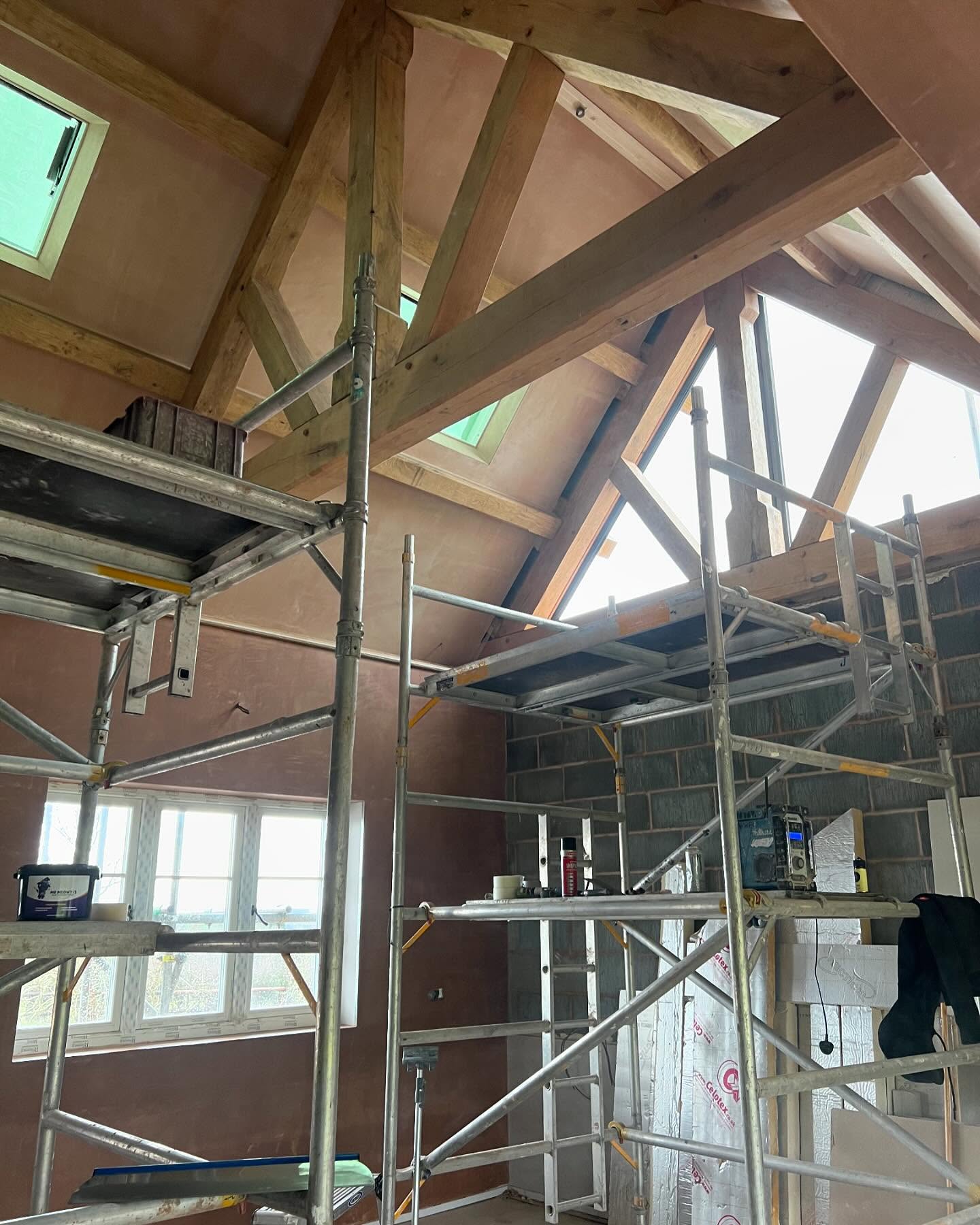 A vaulted oak-beamed room with scaffold towers during plastering