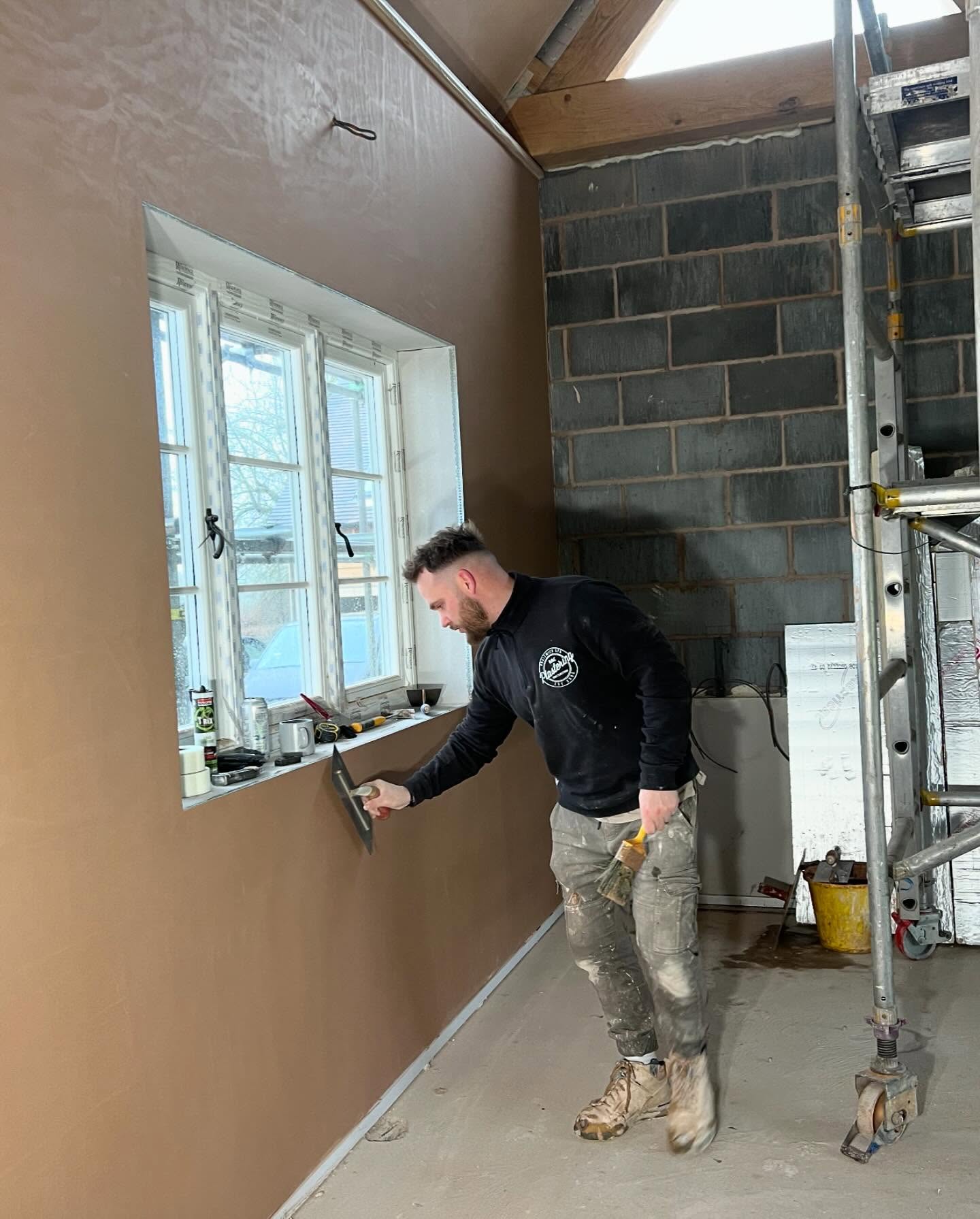 One of the team skimming a wall by a window, scaffold behind